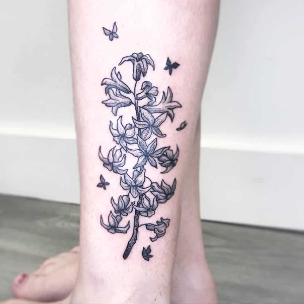 Delicate black and grey tattoo of a lilac branch with fine-line details, surrounded by small fluttering butterflies on the leg.