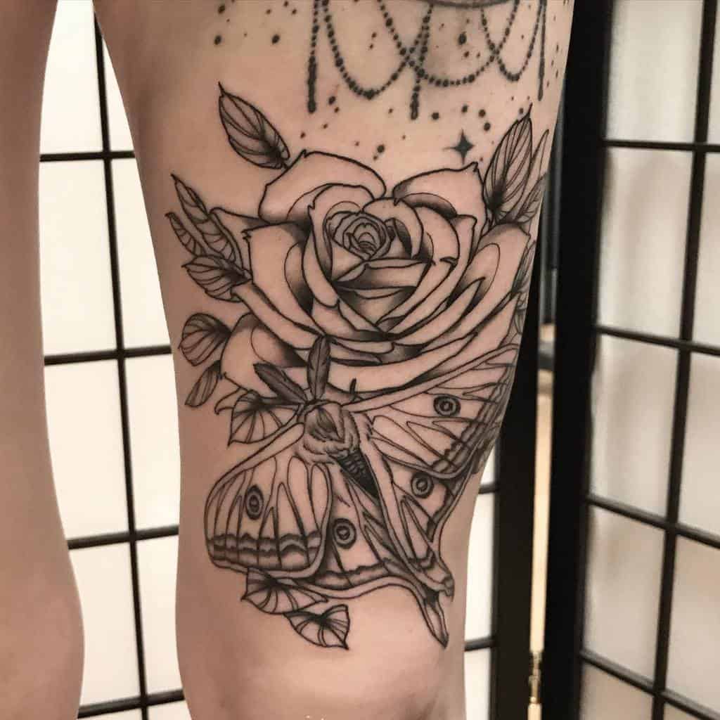 A black and grey tattoo of a Luna Moth with a rose and stars, featuring delicate linework and shading