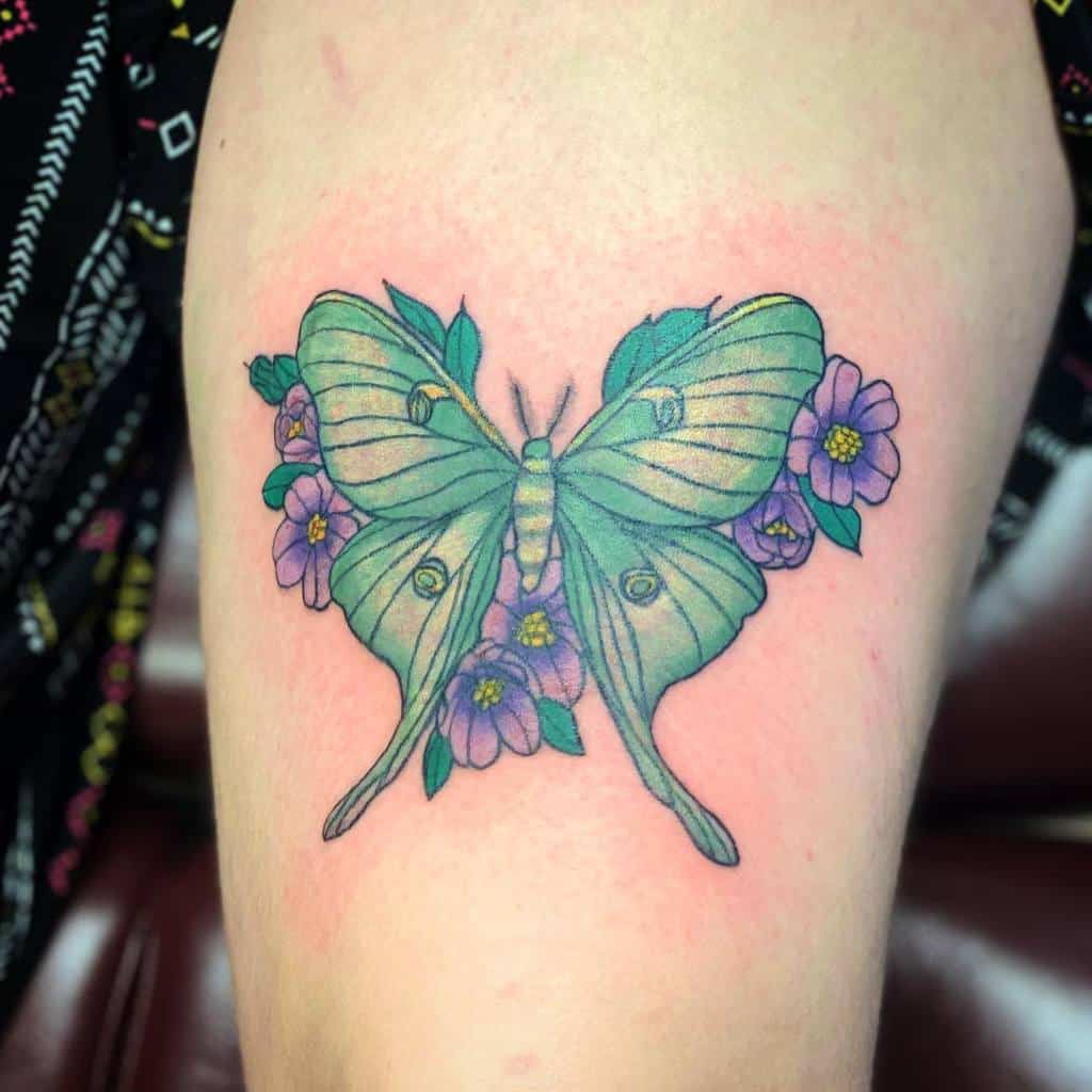 A colorful tattoo of a Luna Moth surrounded by purple flowers, with soft green and purple shading