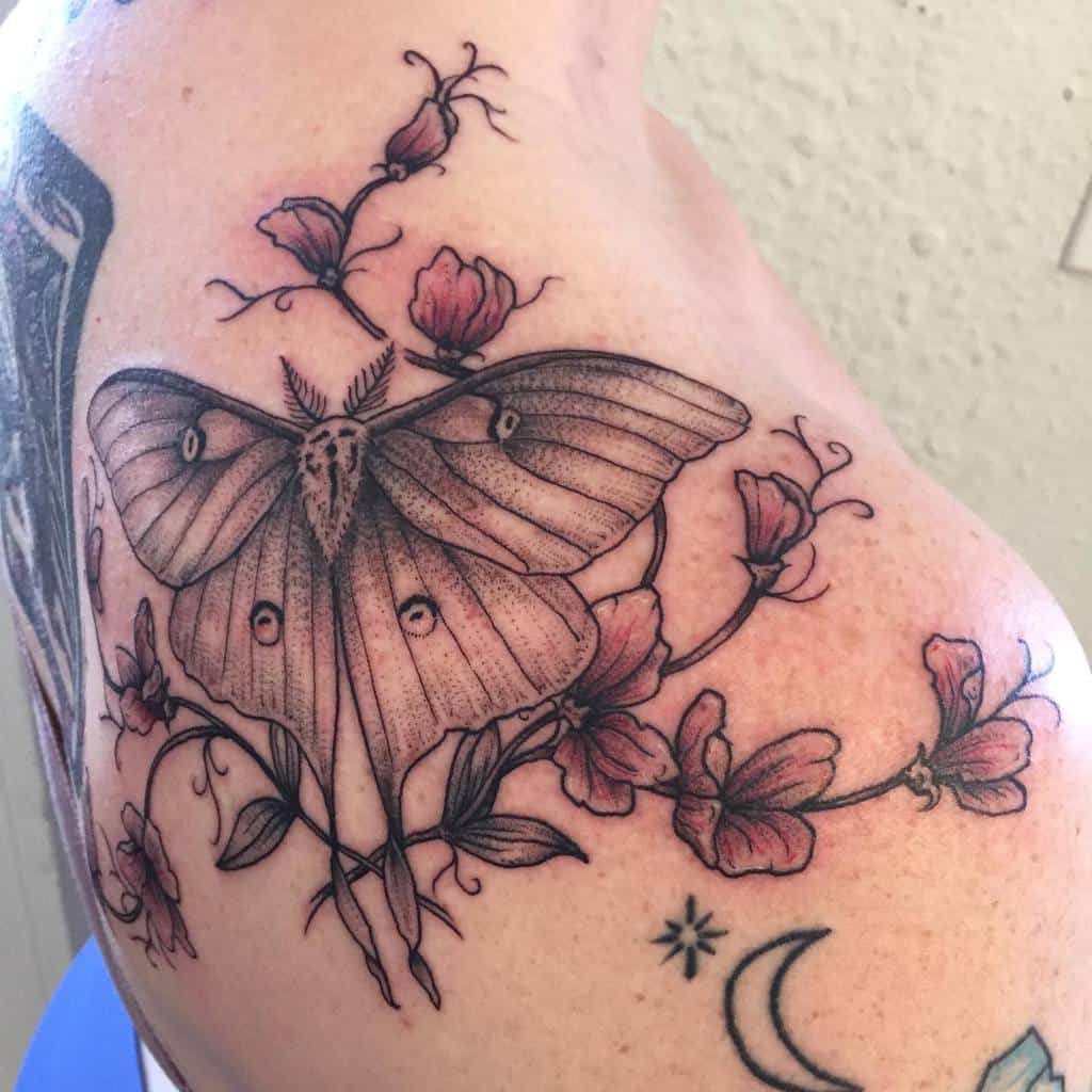 A black and grey tattoo of a Luna Moth surrounded by delicate flowers, with fine line details and shading