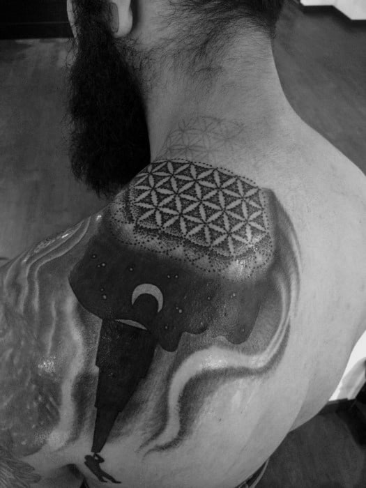 Black and gray tattoo featuring a man looking into a telescope, with the other side forming a face adorned with a geometric pattern, blending cosmic and abstract elements on the shoulder