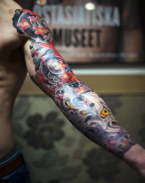 Colorful Japanese-style sleeve tattoo on a man's arm featuring flowers and waves