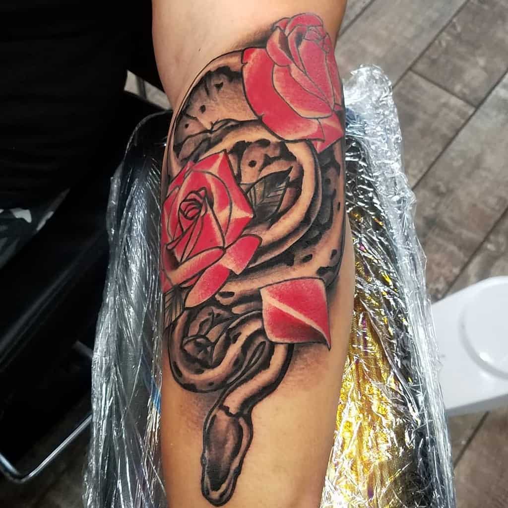 Tattoo of a black snake intertwined with red roses on an arm