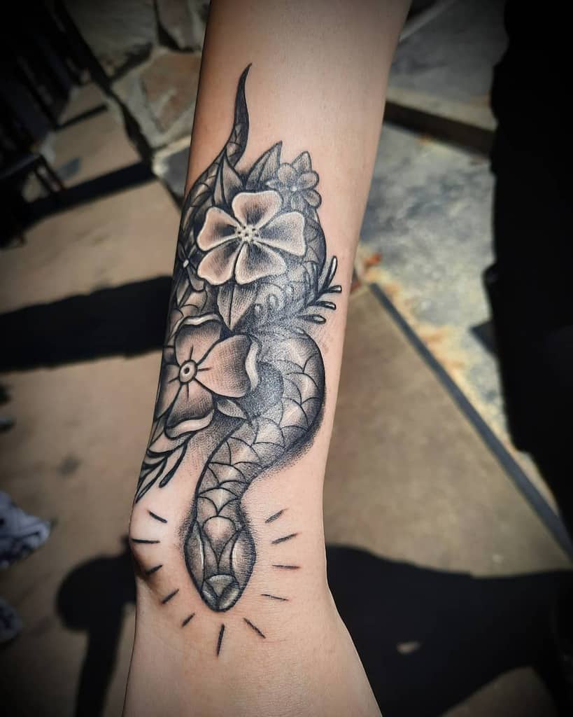 Tattoo of a snake entwined with blooming flowers on an arm