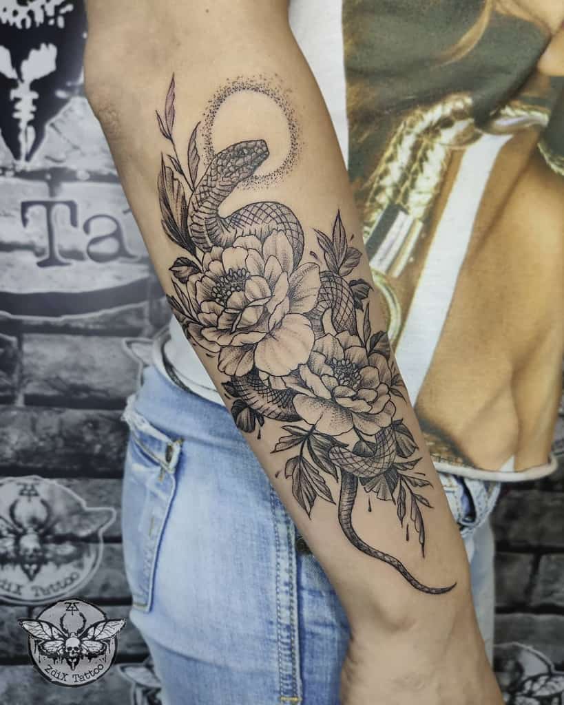 Forearm tattoo of a snake intertwined with flowers and leaves in black ink