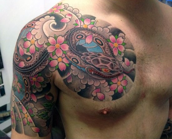 Man showcasing a tattoo of a colorful snake intertwined with cherry blossoms on his chest and shoulder