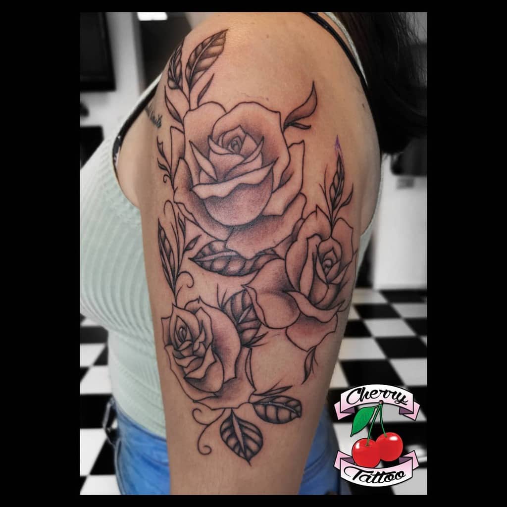 Arm tattoo of shaded roses and leaves on a woman's upper arm