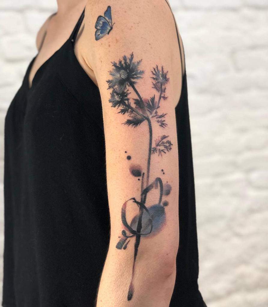 Upper arm tattoo of a tall flower with abstract shapes and a blue butterfly on the shoulder