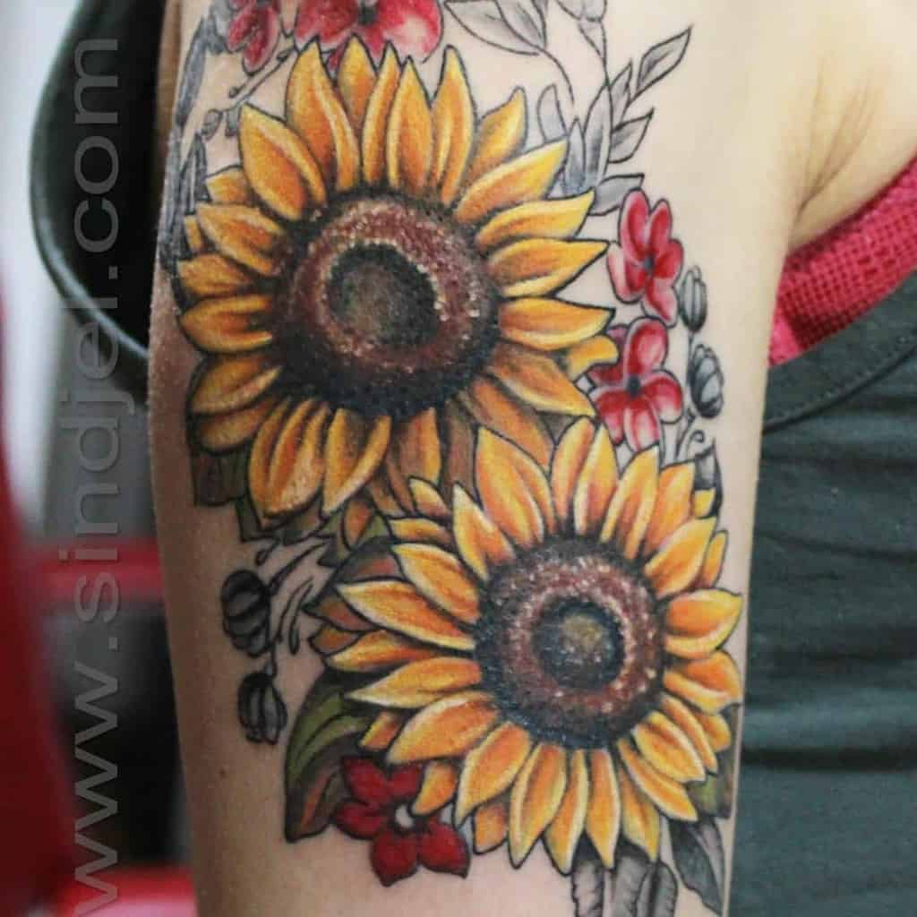 Tattoo of two sunflowers with red flowers and leaves on an upper arm