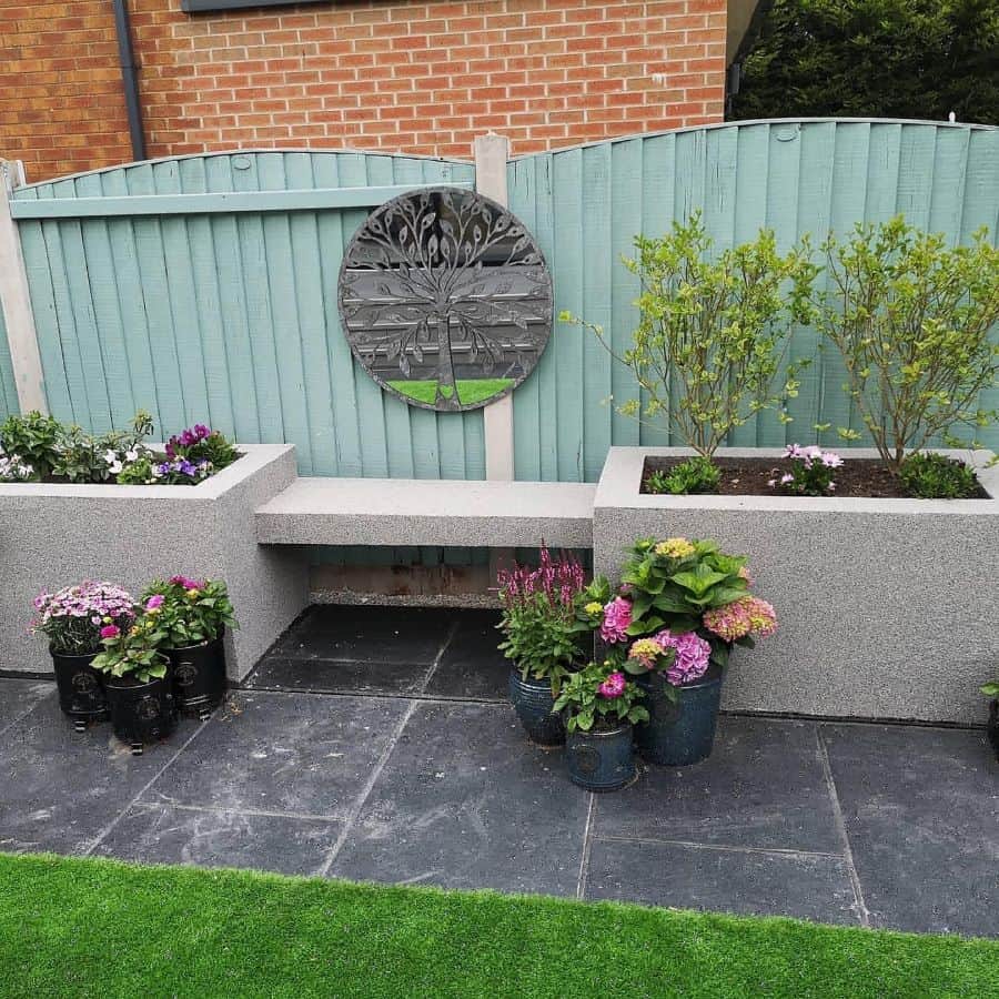 raised stone flower bed with bench green wood fence pot plants