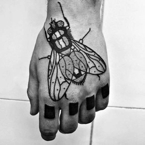 Bold linework fly tattoo covering the top of the hand, featuring stylized wings and dotted details with solid black fingertips.