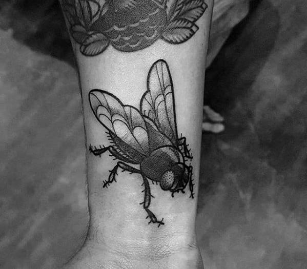 Black and grey fly tattoo on the wrist with detailed shading and realistic texture, capturing the insect's natural look.