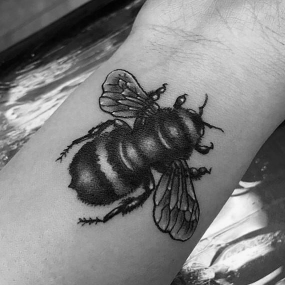 Black and grey bee tattoo with bold shading, textured body, and detailed wings, placed on the forearm for a striking look.