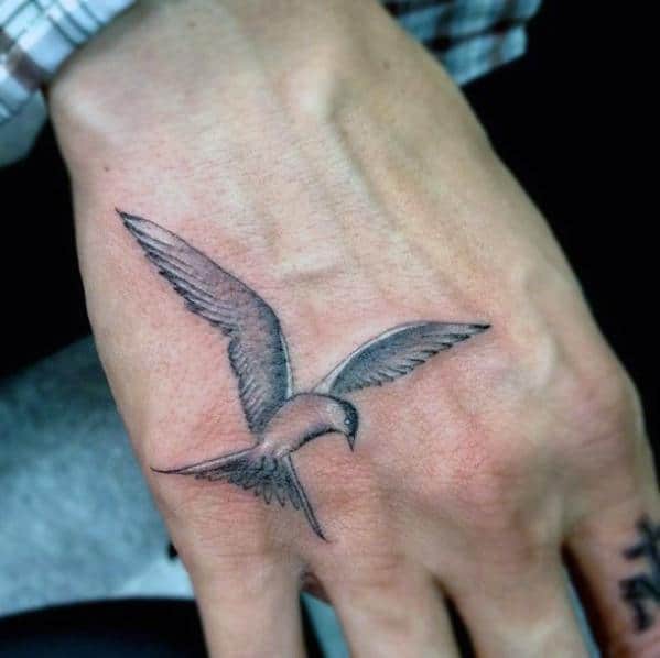 Tattoo of a bird in flight on the back of a person's hand