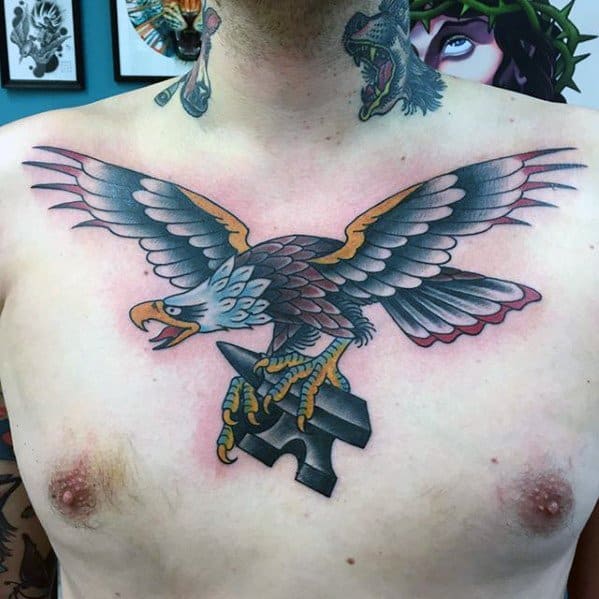 Traditional eagle tattoo across the chest with wings spread wide, clutching a black anvil in its talons, bold colors and shading throughout.