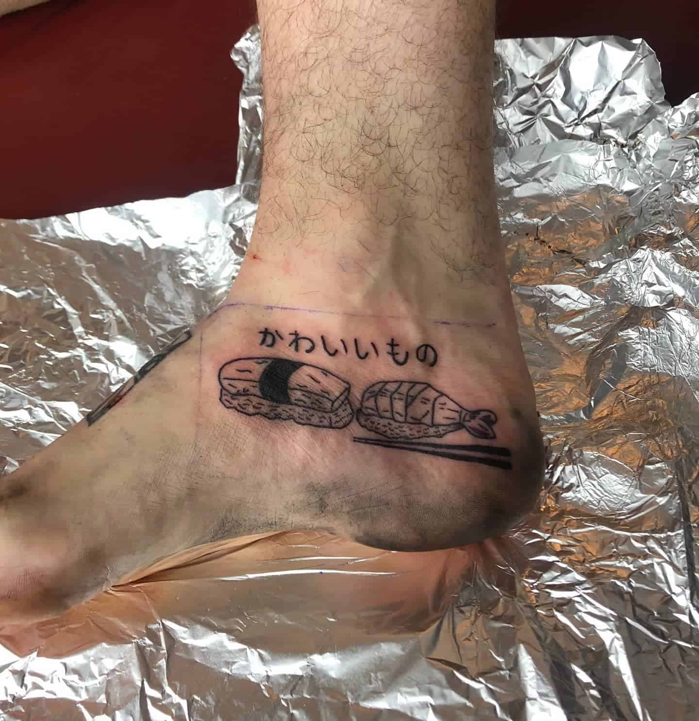 Black ink tattoo featuring sushi and a piece of candy, with the Japanese text 'かわいいものの' (cute things) above the design