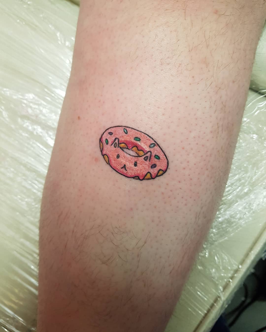 A small tattoo of a pink frosted donut with sprinkles