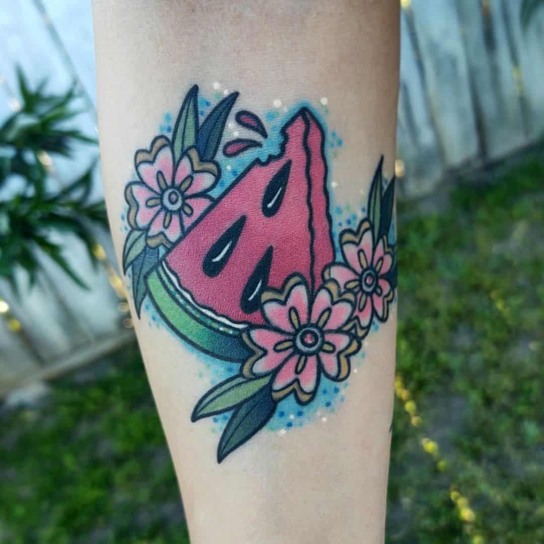 Tattoo of a watermelon slice decorated with pink flowers and green leaves with blue background
