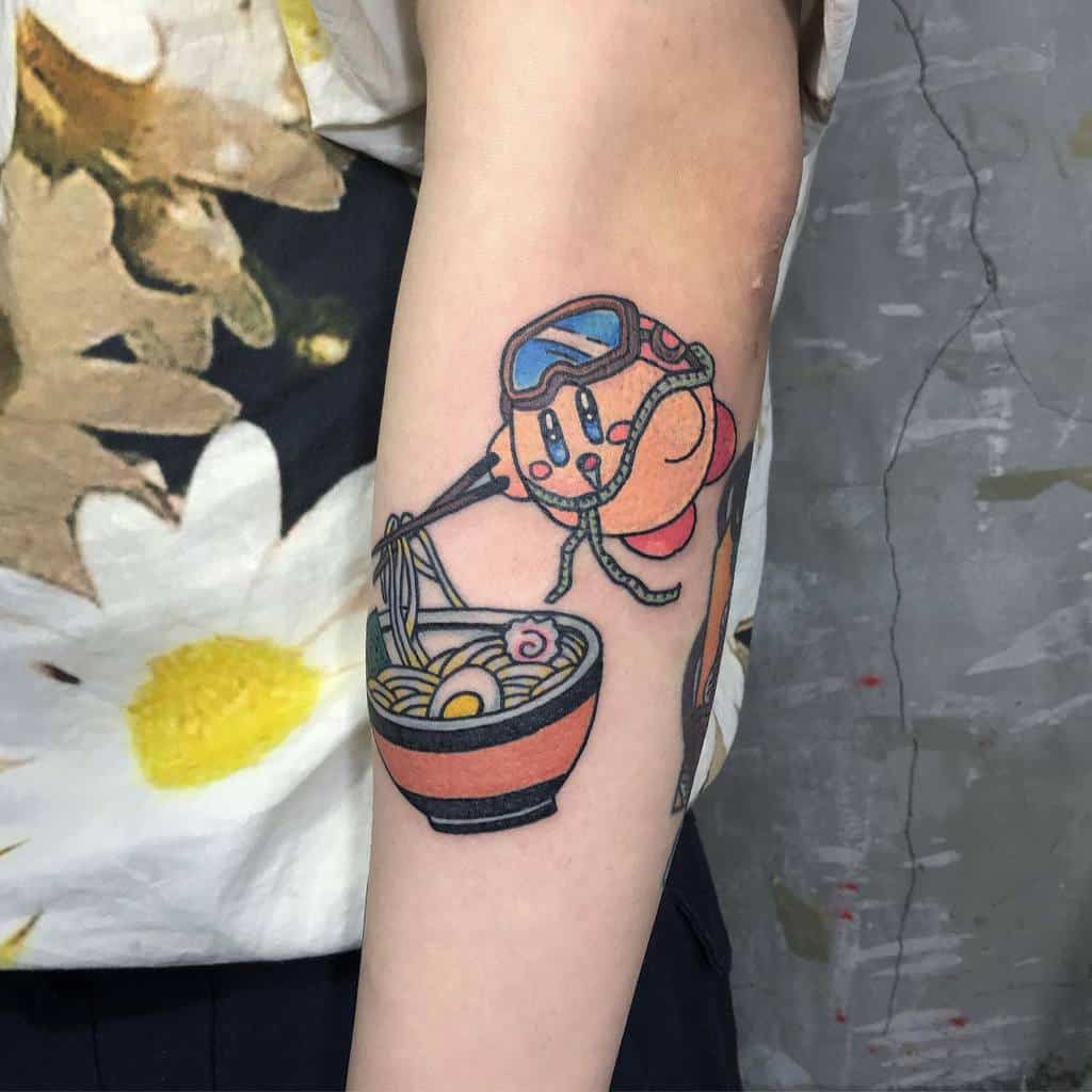 Kirby tattoo wearing goggles and slurping noodles from a ramen bowl with chopsticks and surrounded by rope