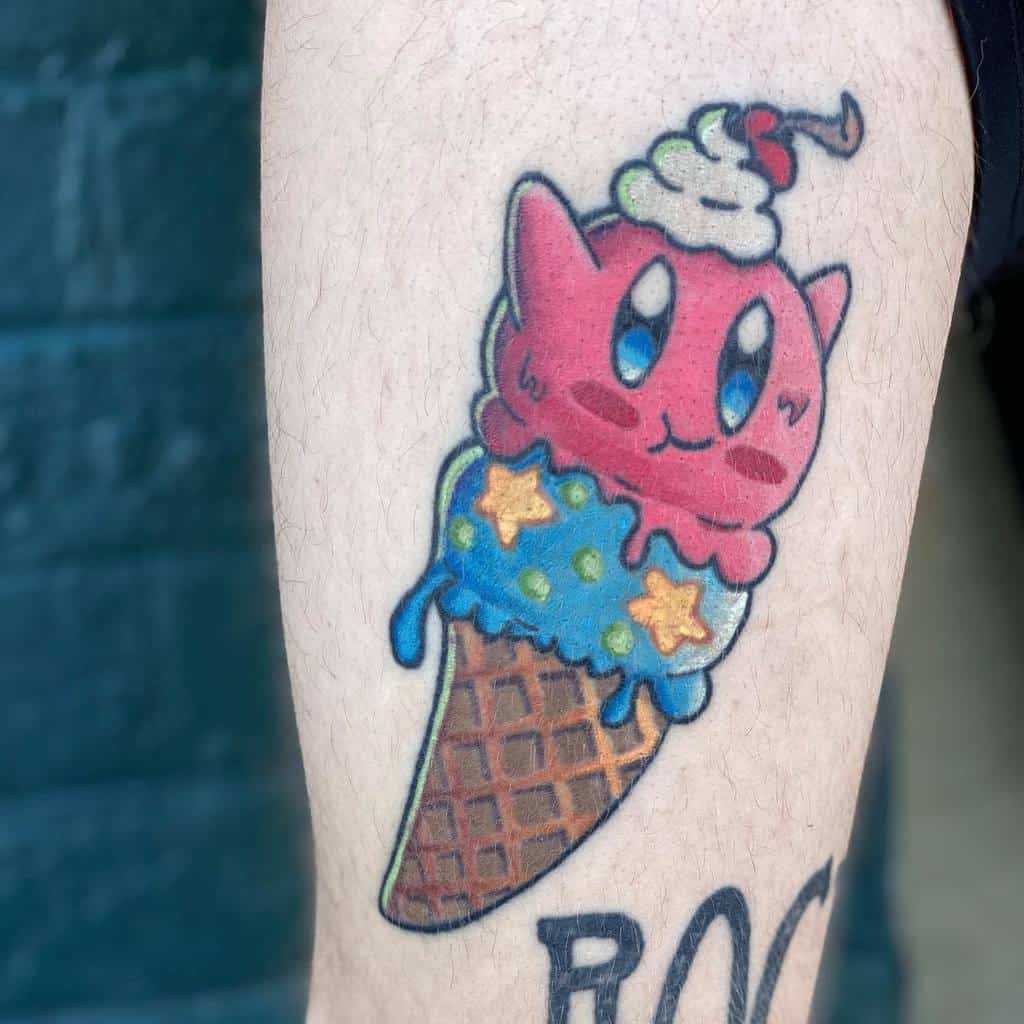 Kirby tattoo designed as an ice cream cone, with blue frosting, star-shaped sprinkles, whipped cream, and a cherry on top