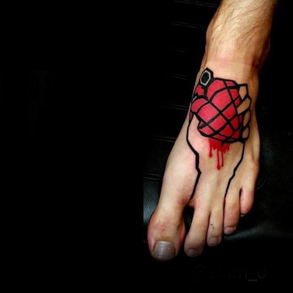 Tattoo of Green Day’s red hand grenade heart logo with dripping blood effect, inked on the top of the foot in bold lines.