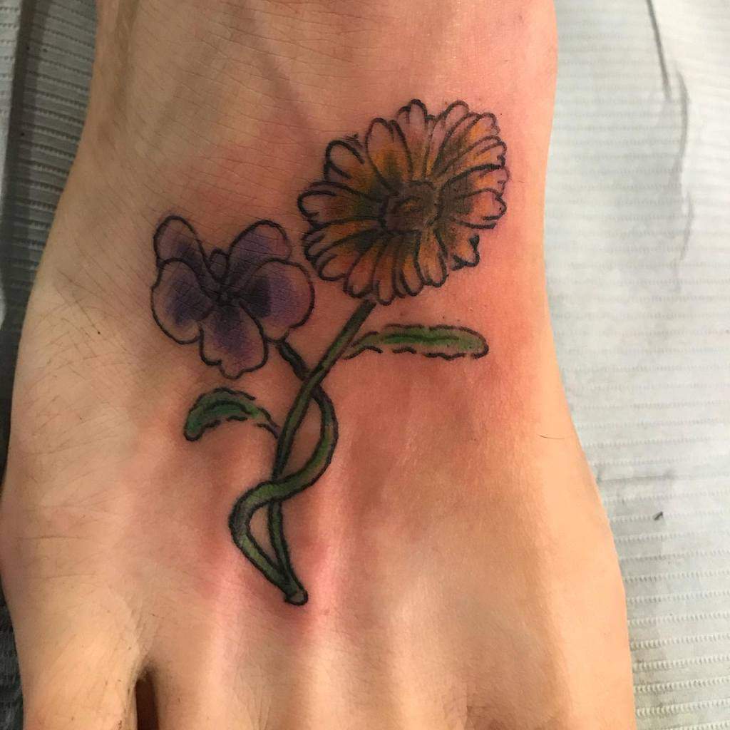 Foot tattoo featuring a delicate violet flower intertwined with a vibrant yellow daisy, symbolizing balance, nature, and resilience