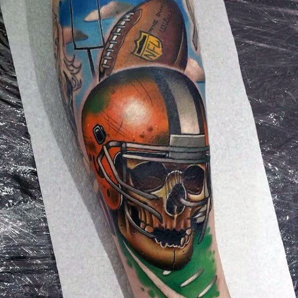 Vibrant tattoo of a football helmet with a skull inside, an NFL ball, and field background, blending sports and dark art elements.