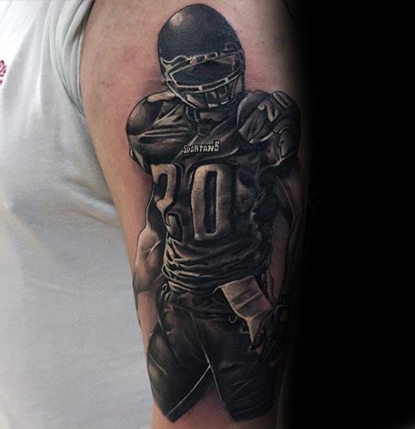 Realistic black and grey tattoo of a football player in full gear with the number 20 and "Spartans" on the jersey.