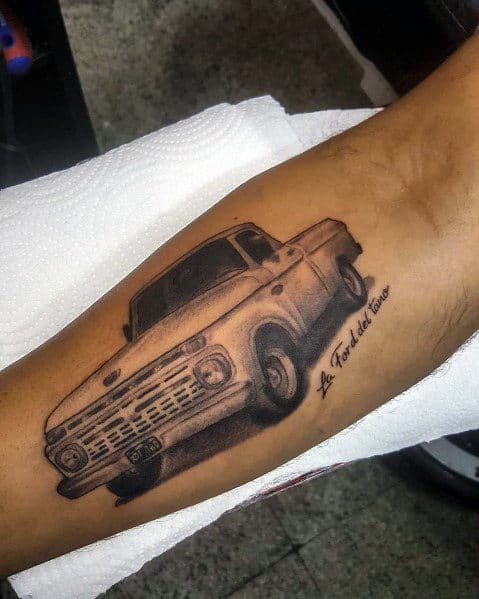 Black and grey Ford pickup truck tattoo on forearm, featuring a vintage design with realistic shading and the phrase "La Ford del abuelo."