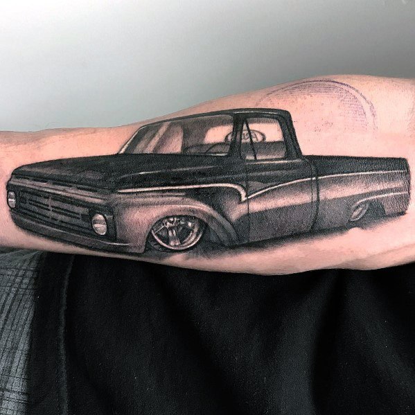 Realistic black and grey Ford pickup truck tattoo on forearm, featuring fine shading, sleek details, and a lowered custom design.