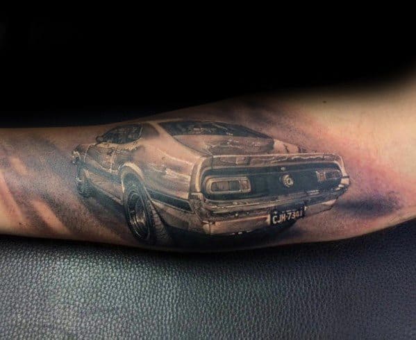 Realistic black and grey Ford Mustang tattoo on forearm, showcasing a detailed rear view with intricate shading and a vintage muscle car design.