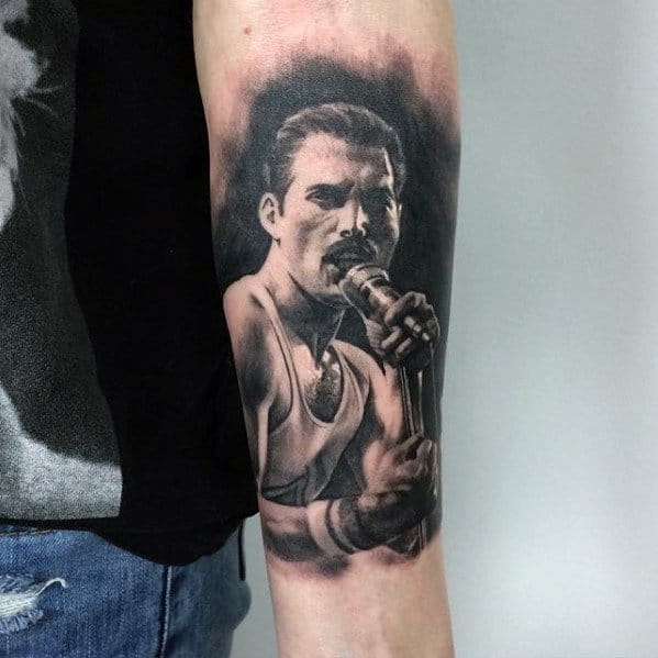 Realistic black and grey forearm tattoo of Freddie Mercury holding a microphone in classic Live Aid pose with intense expression.