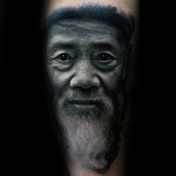 A realistic tattoo of an elderly man's face with a long beard and kind expression