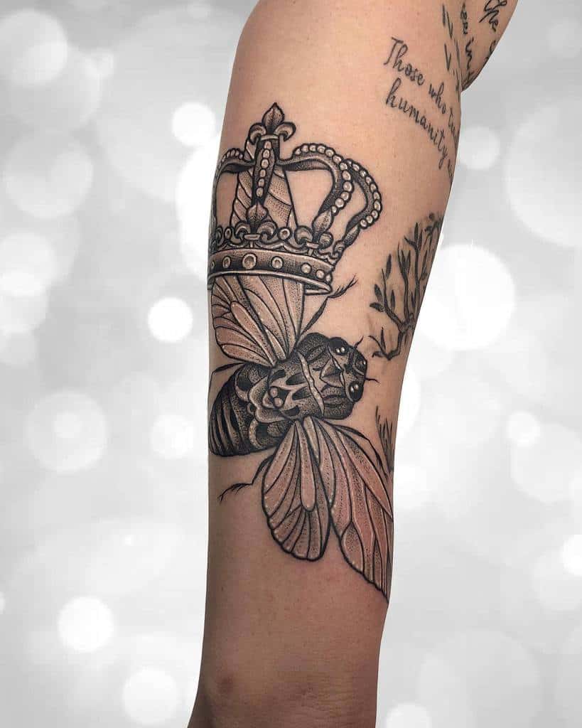 Black and grey tattoo of a cicada with a detailed crown on its back, featuring fine shading and intricate linework
