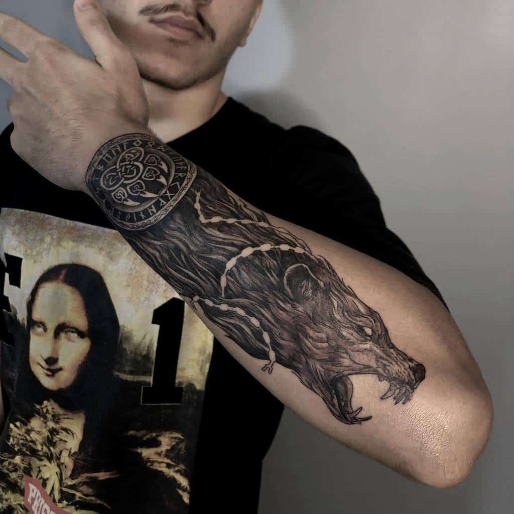 Forearm tattoo of a detailed Norse wolf design, featuring intricate fur and chain elements, paired with a circular Viking symbol on the wrist