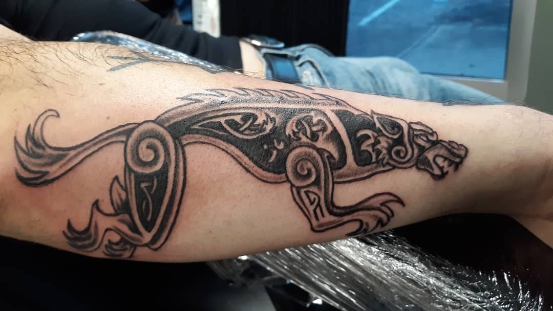 Forearm tattoo of Fenrir in a bold Nordic knotwork design, featuring intricate curves and traditional patterns
