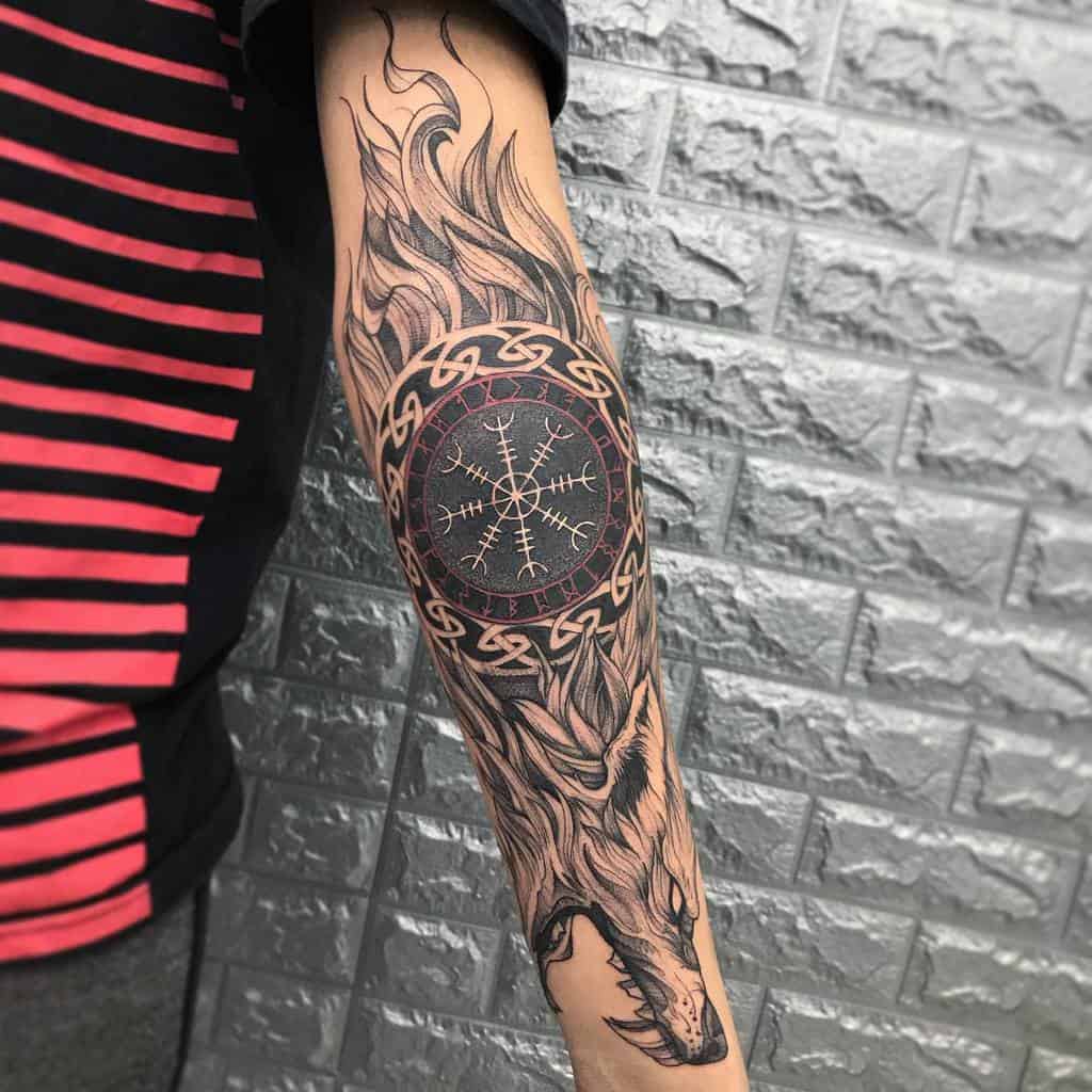 Forearm tattoo featuring a Norse-inspired design with a Vegvisir symbol encircled by Celtic knots, flames, and a wolf's head
