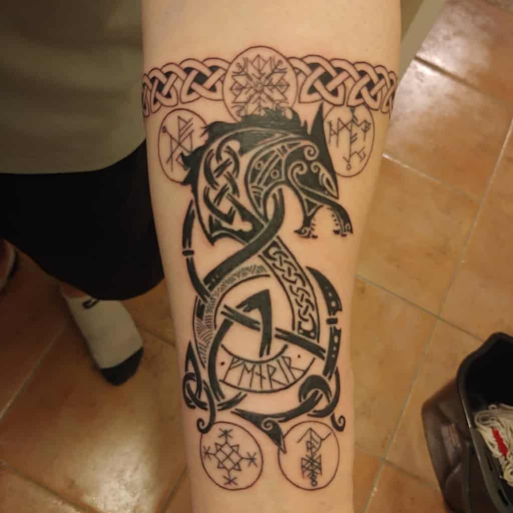 Forearm tattoo showcasing Fenrir in a traditional Norse knotwork style, surrounded by intricate runes and a Celtic band