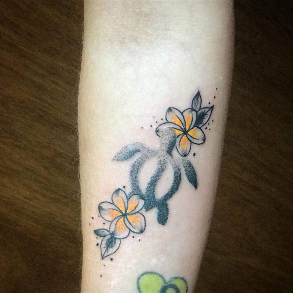 Tattoo of a turtle with yellow plumeria flowers and leaves on an arm