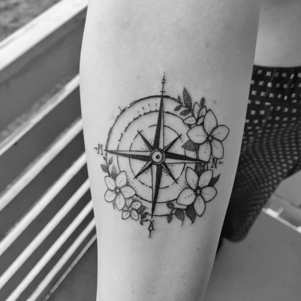 Tattoo of a compass with plumeria flowers on a person's arm in black and white