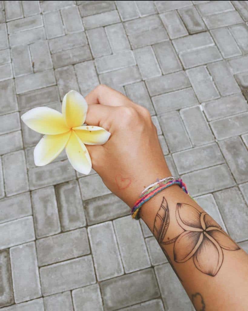 Hand holding a white and yellow plumeria with a matching tattoo on the wrist