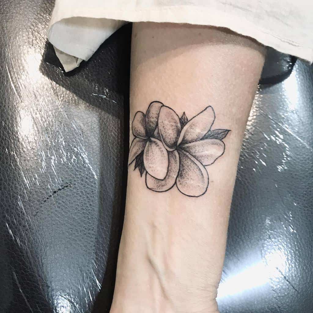 Black and gray plumeria flower tattoo on an arm