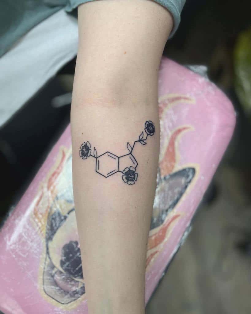 Tattoo of a serotonin molecule with delicate floral accents adorning a forearm