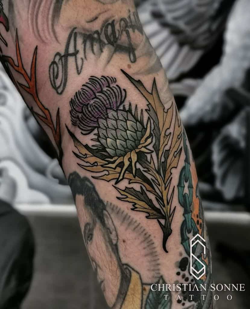 A tattooed arm elegantly showcases a blooming thistle amidst intricate designs