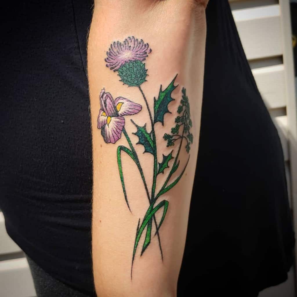 A vibrant tattoo of a purple thistle intertwined with a pink iris and lush green leaves elegantly graces the person’s arm