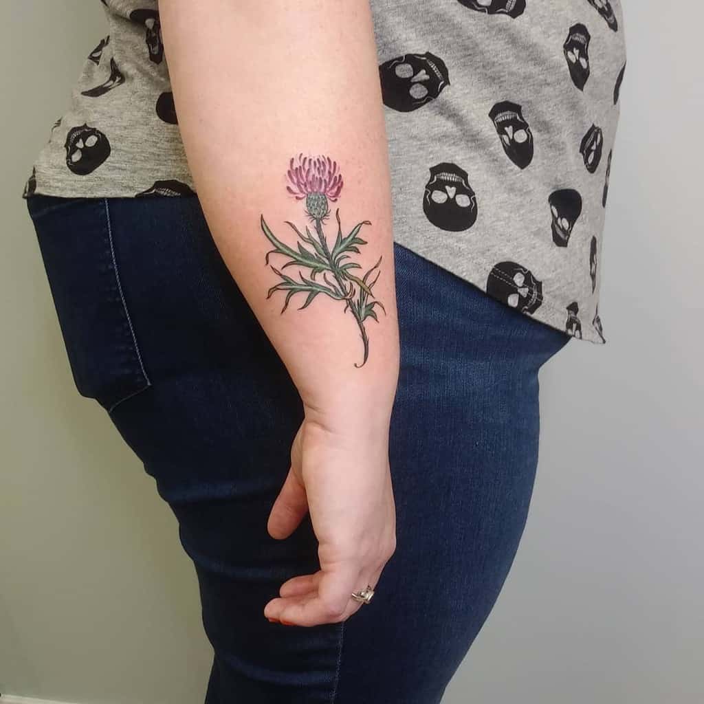 Simple and colorful forearm tattoo of a pink thistle flower with green leaves, showcasing natural elegance