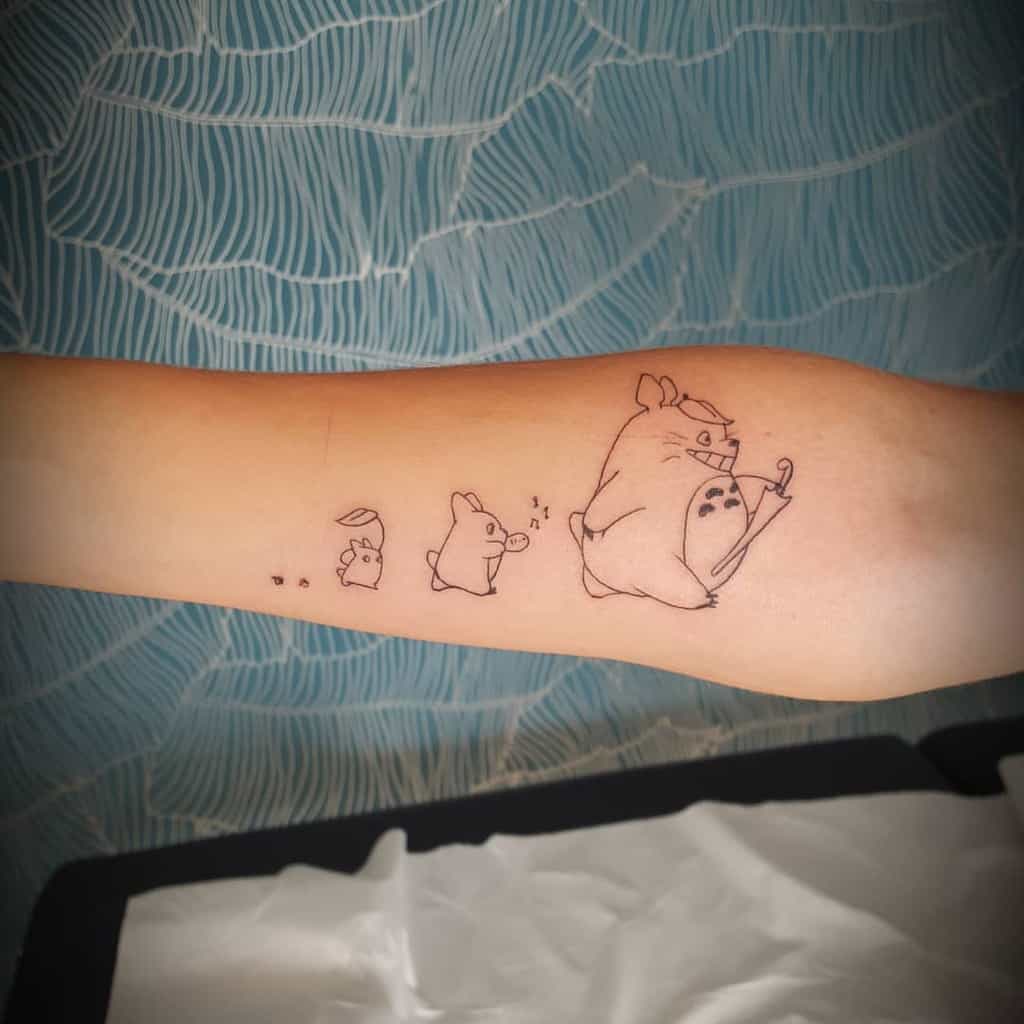 Forearm tattoo of Totoro showing him in a progression from small to large, in minimalist line art