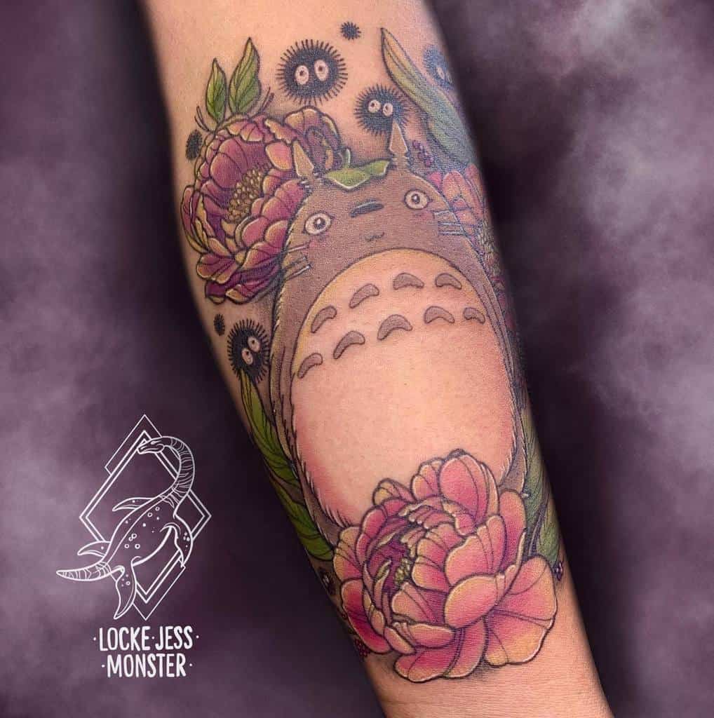 Detailed Totoro tattoo on the forearm, featuring Totoro surrounded by vibrant pink peonies, green leaves, and playful soot sprites