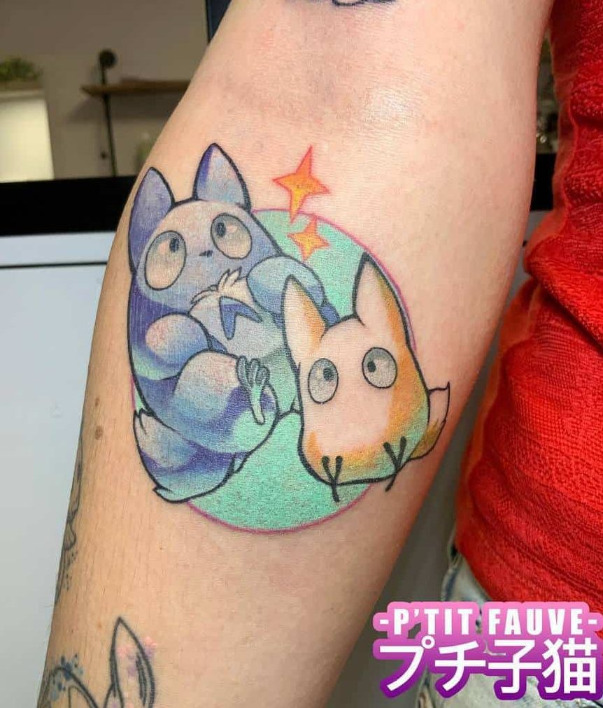 Cute Totoro-inspired tattoo featuring blue and pink mini Totoros within a pastel circle, with sparkles above them