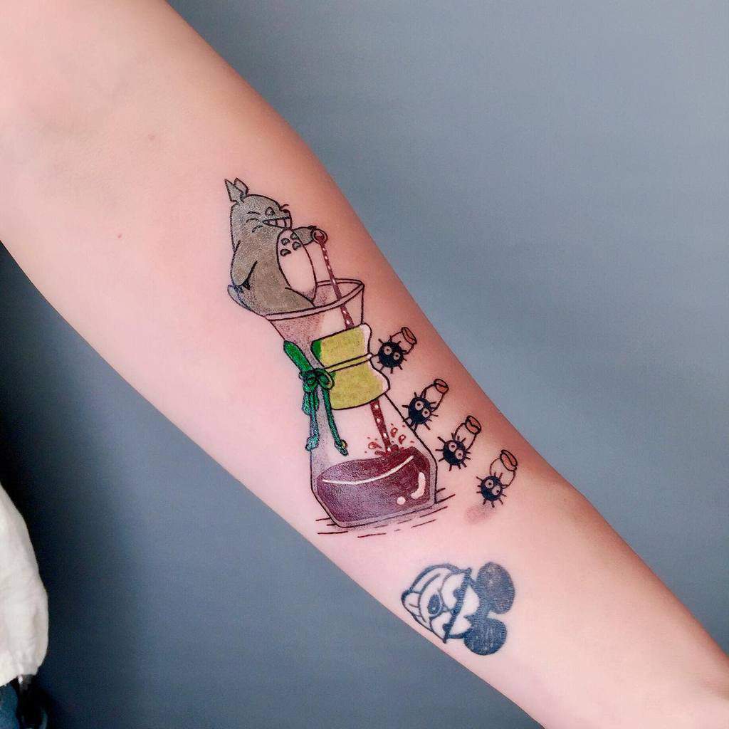 A playful Totoro tattoo design showing Totoro perched on top of a coffee pour-over, with soot sprites tumbling out of the carafe